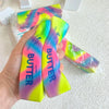 A hand holds a rainbow colored butter stick squishy fidget toy with bright yellow and pink hues.