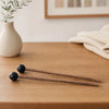 A pair of wooden handpan drum mallets with silicone tips resting on a wooden surface.