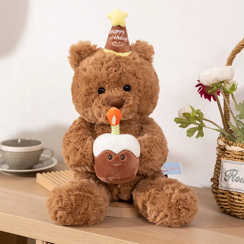 A fluffy brown teddy bear plush toy with an eye mask and a small birthday cake on its chest.