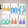 A set of eight polymer clay jewelry findings featuring floral texture roller designs in various shades of yellow, blue, and p