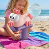 A young girl is holding a pink ant-shaped water blaster toy on a purple launcher on a sandy beach.