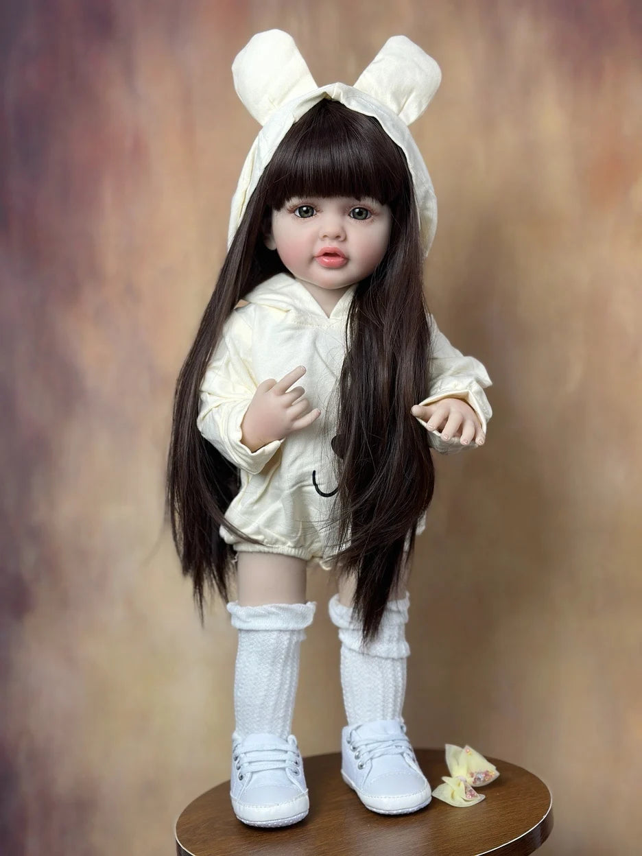 A lifelike 55 cm soft silicone baby doll with long dark hair and white ears wearing a cream outfit.