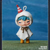 A white hooded doll with blue hair and a striped party hat stands on green grass.