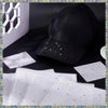 A black baseball cap is shown next to white rhinestone sticker sheets and a white geometric object.
