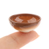 A small, brown ceramic rice bowl is held by a hand against a white background.