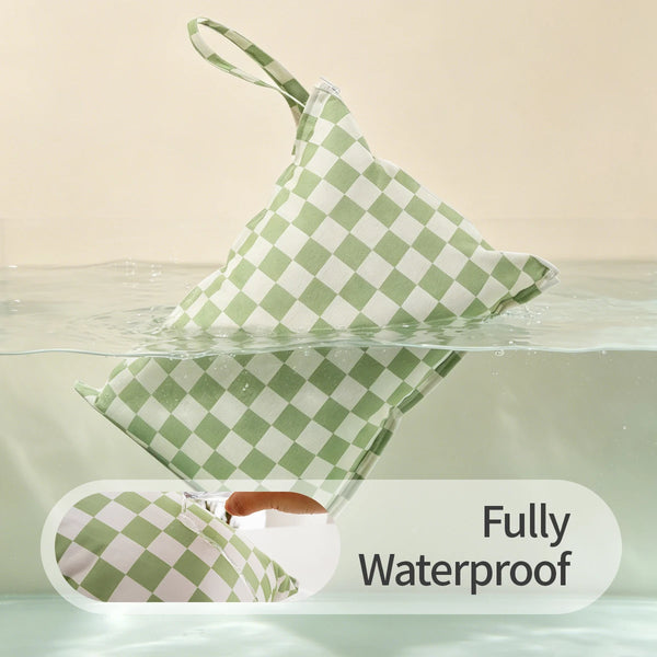 A green and white checkered reusable zipper diaper cover floating in water, demonstrating its waterproof feature.