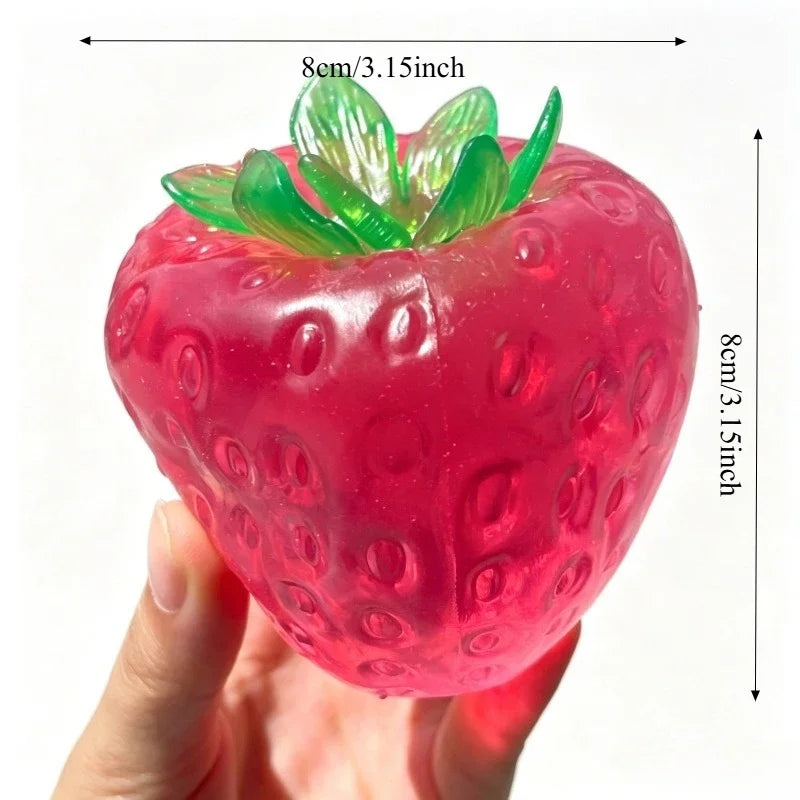 A bright pink squishy strawberry stress ball with green leaves is held in a hand.