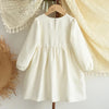 A cream-colored girls' long sleeve A-line dress with a bow detail hanging on a wooden hanger.