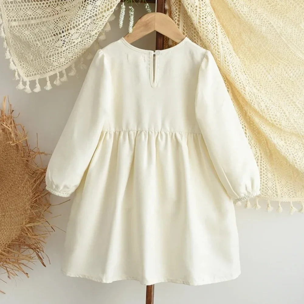 A cream-colored girls' long sleeve A-line dress with a bow detail hanging on a wooden hanger.
