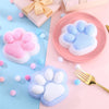 Pink and blue squishy cat paw toys resting on a pink surface with a gold fork.