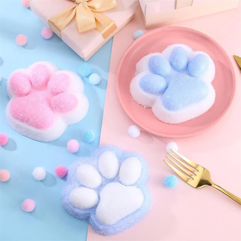 Pink and blue squishy cat paw toys resting on a pink surface with a gold fork.