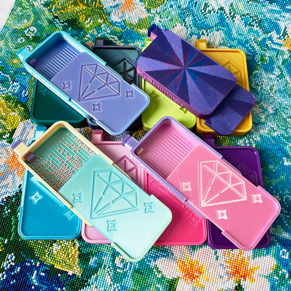 A collection of diamond painting organizer trays in various colors, including purple, pink, teal, and yellow, arranged on a c
