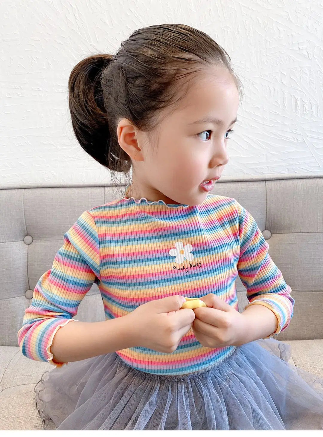 A young girl wearing a colorful striped floral print long-sleeved shirt and a gray tulle skirt.