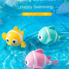 A colorful wind-up swimming duck fish toy in yellow, green, and pink floating in blue water.