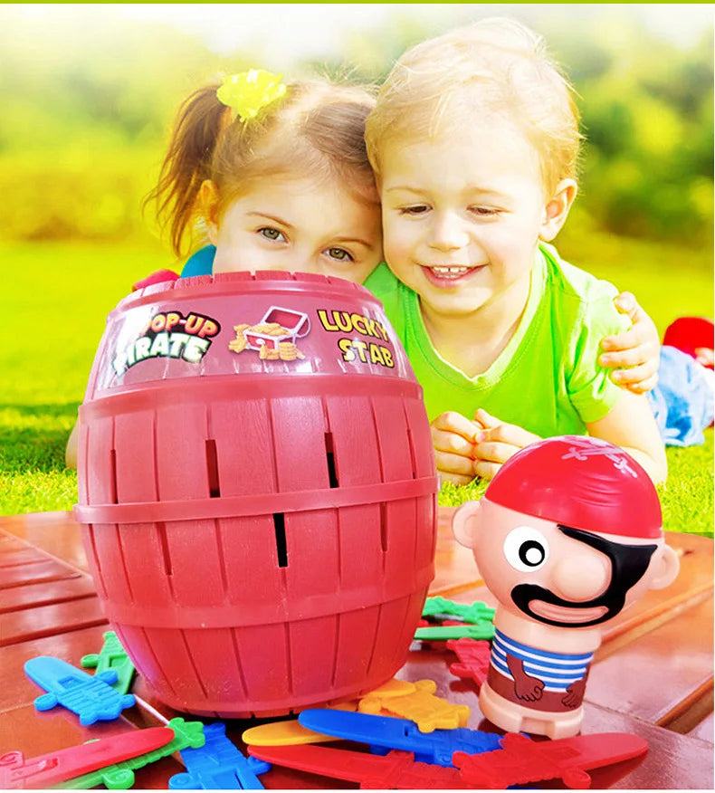 A young child is holding a red pirate barrel game with a sword stab piece on a wooden table.
