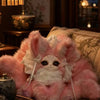 A pink fox plush collectible with white fur and lace details resting on a brown sofa.