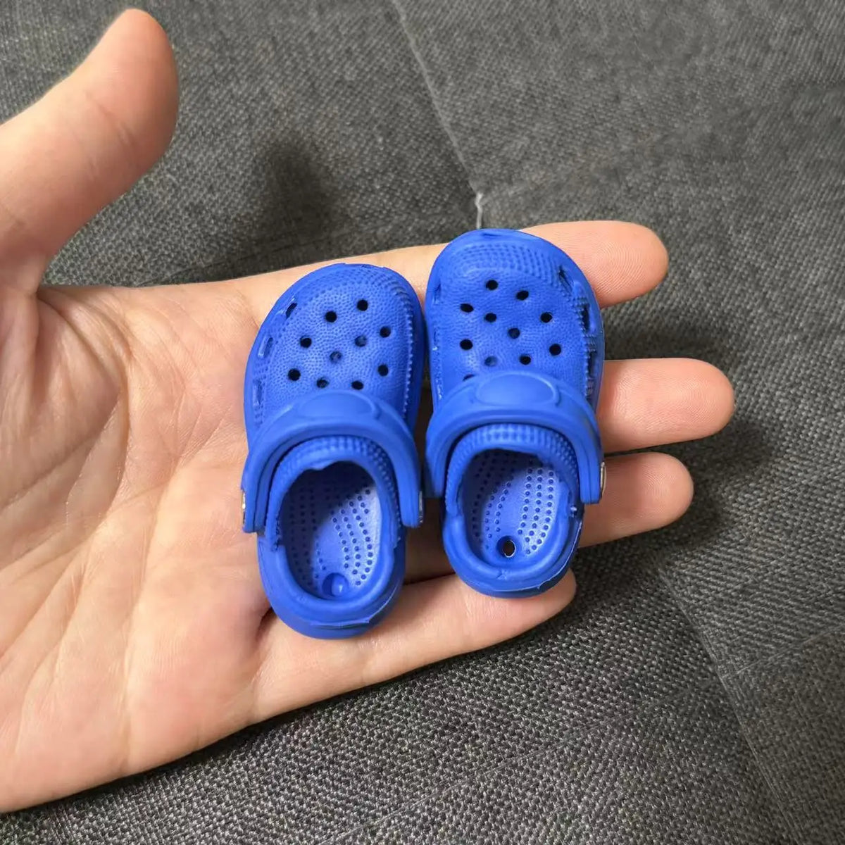 A pair of blue fashion slippers for 1/6 BJD dolls held in a person's hand.