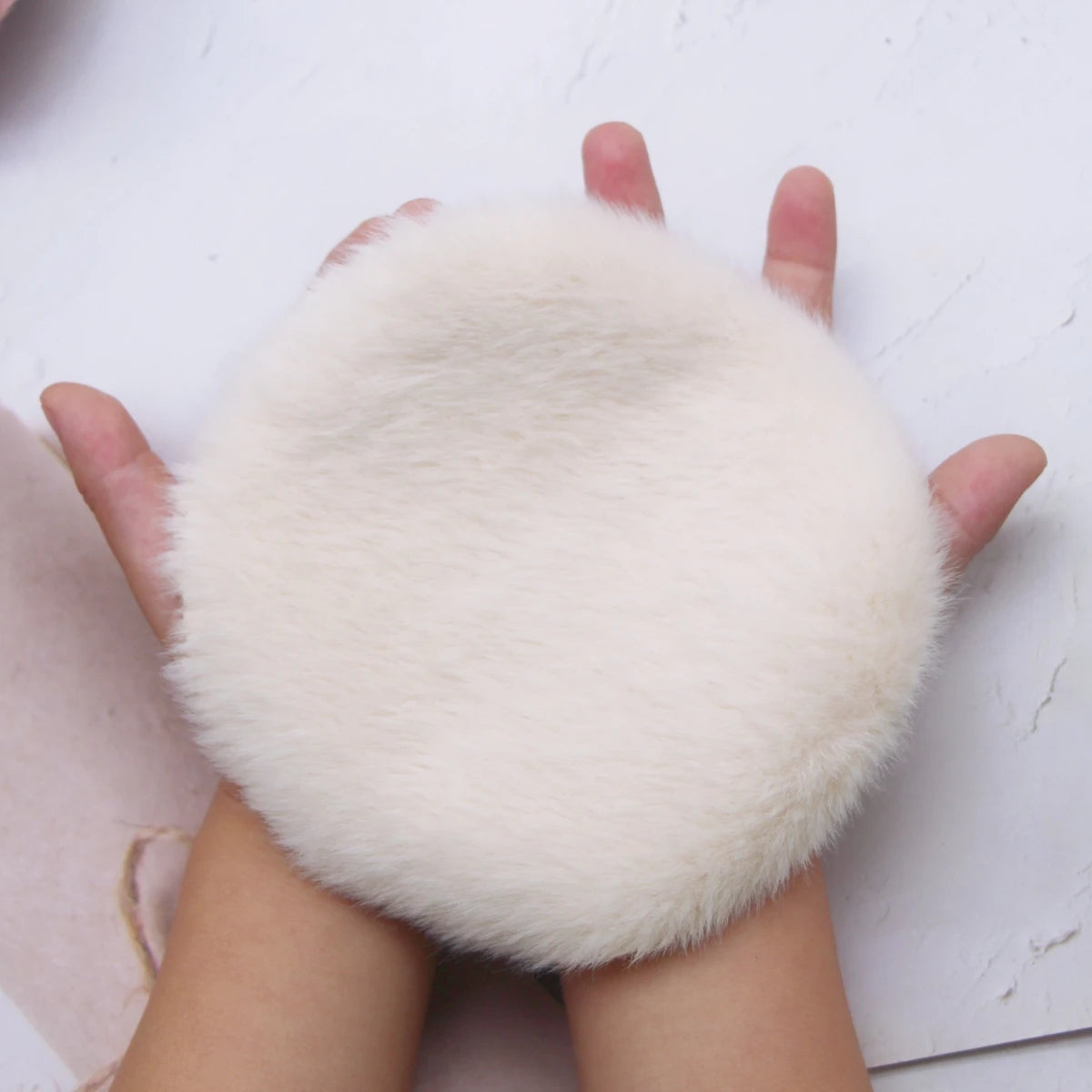 A hand is holding a fluffy white miniature carpet mat for dollhouse decor.