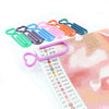 A collection of heart-shaped canvas clips in various colors, including green, purple, blue, and orange, laid out on a pink fa