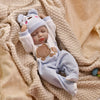 A baby doll wearing a light blue animal romper and matching hat, lying on a beige knitted blanket.