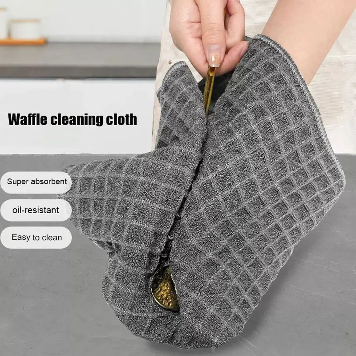A hand is holding a gray waffle cleaning cloth, demonstrating its absorbent and oil-resistant features.