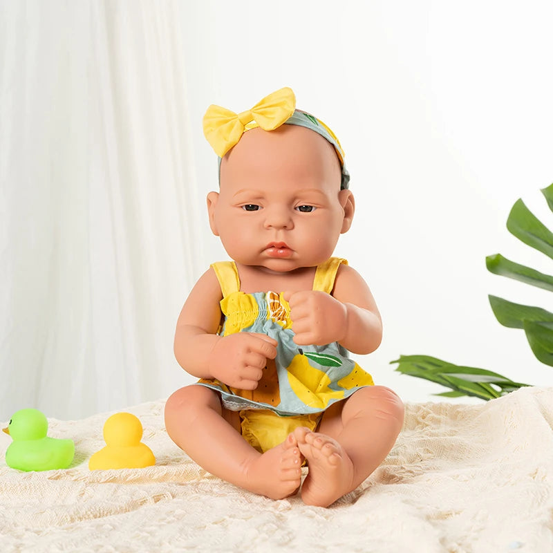 A lifelike vinyl reborn doll with a yellow bow and outfit sitting on a white textured surface.
