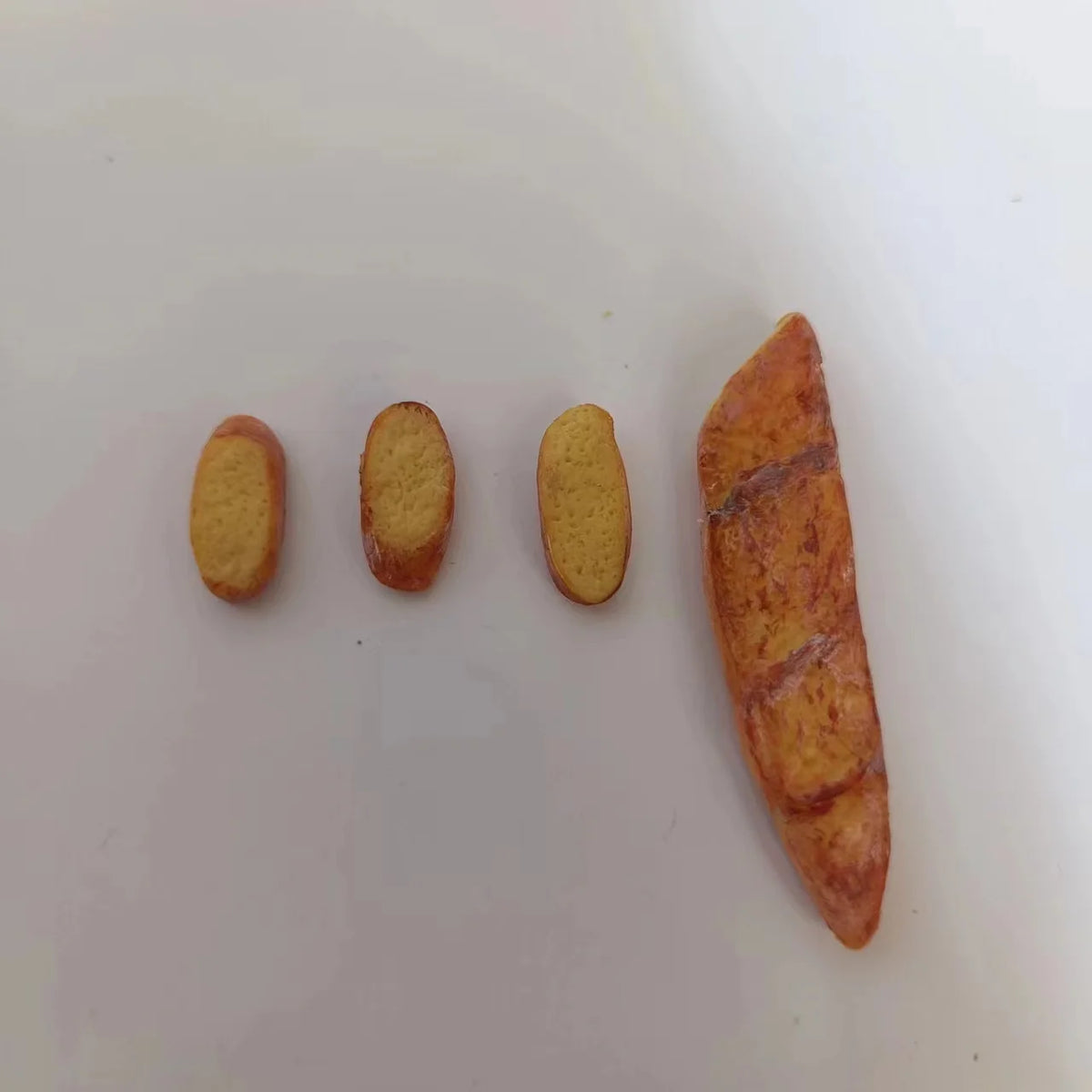 Three miniature baguettes of varying sizes displayed on a white surface.