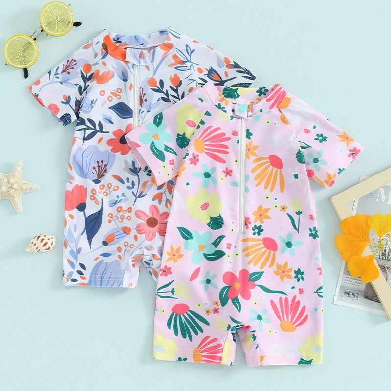 A pink and floral baby rash guard swimsuit with a zipper is displayed on a light blue background.