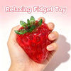 A hand holds a bright red strawberry squishy stress ball with green leaves, used as a relaxing fidget toy.