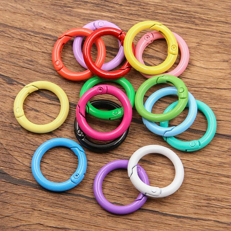 A collection of ten colorful metal O-ring spring clasps in various bright colors arranged on a wooden surface.