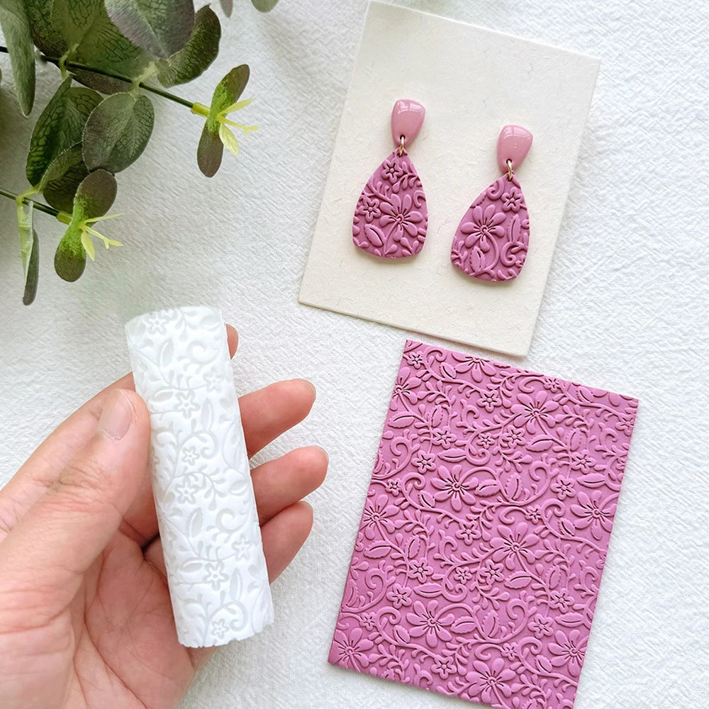 A pair of pink clay texture rollers and a finished piece of jewelry are displayed on a white surface.