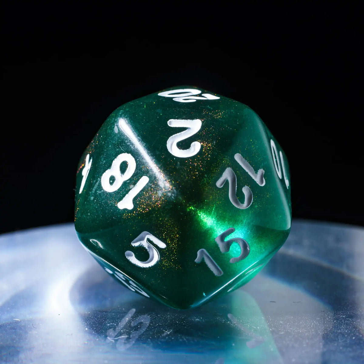 A green translucent polyhedral die with the number 2 is resting on a reflective surface.