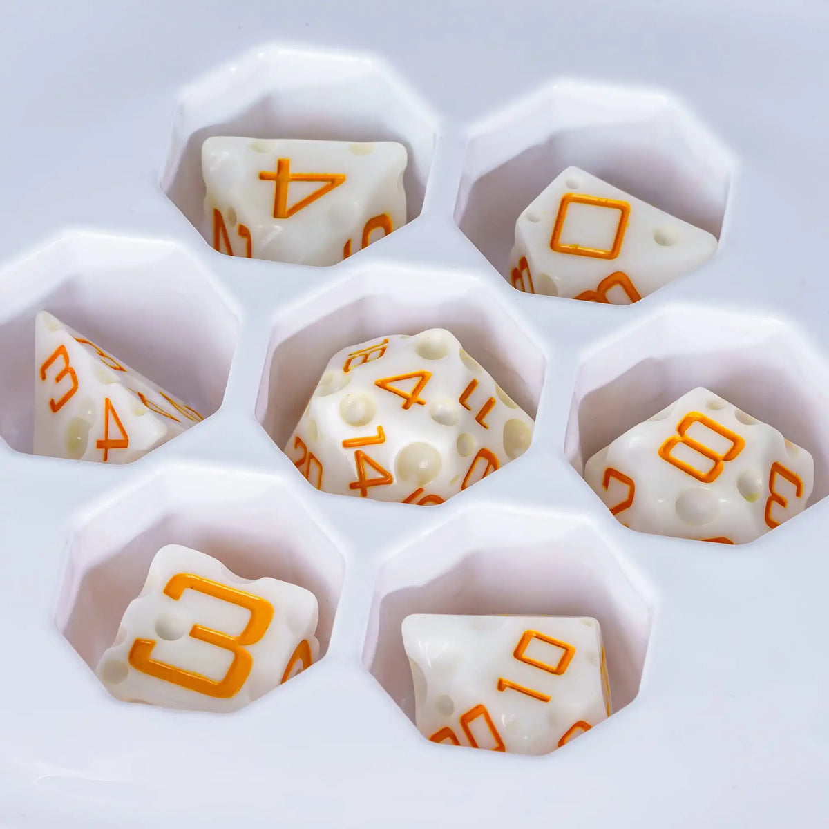 Seven white cheese-shaped polyhedral dice arranged in a hexagonal pattern on a white background.
