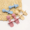 A set of nine silicone baby utensils including forks and spoons in various pastel colors resting on a woven mat.