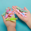 A hand holds several colorful rubber dinosaur slingshot toys, including green, pink, and yellow varieties.