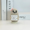 A small, handwoven crochet ornament shaped like a potato with a pink flower detail, sitting on a white surface.