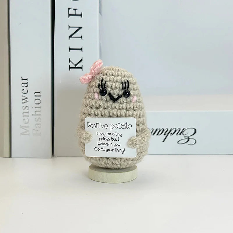 A small, handwoven crochet ornament shaped like a potato with a pink flower detail, sitting on a white surface.