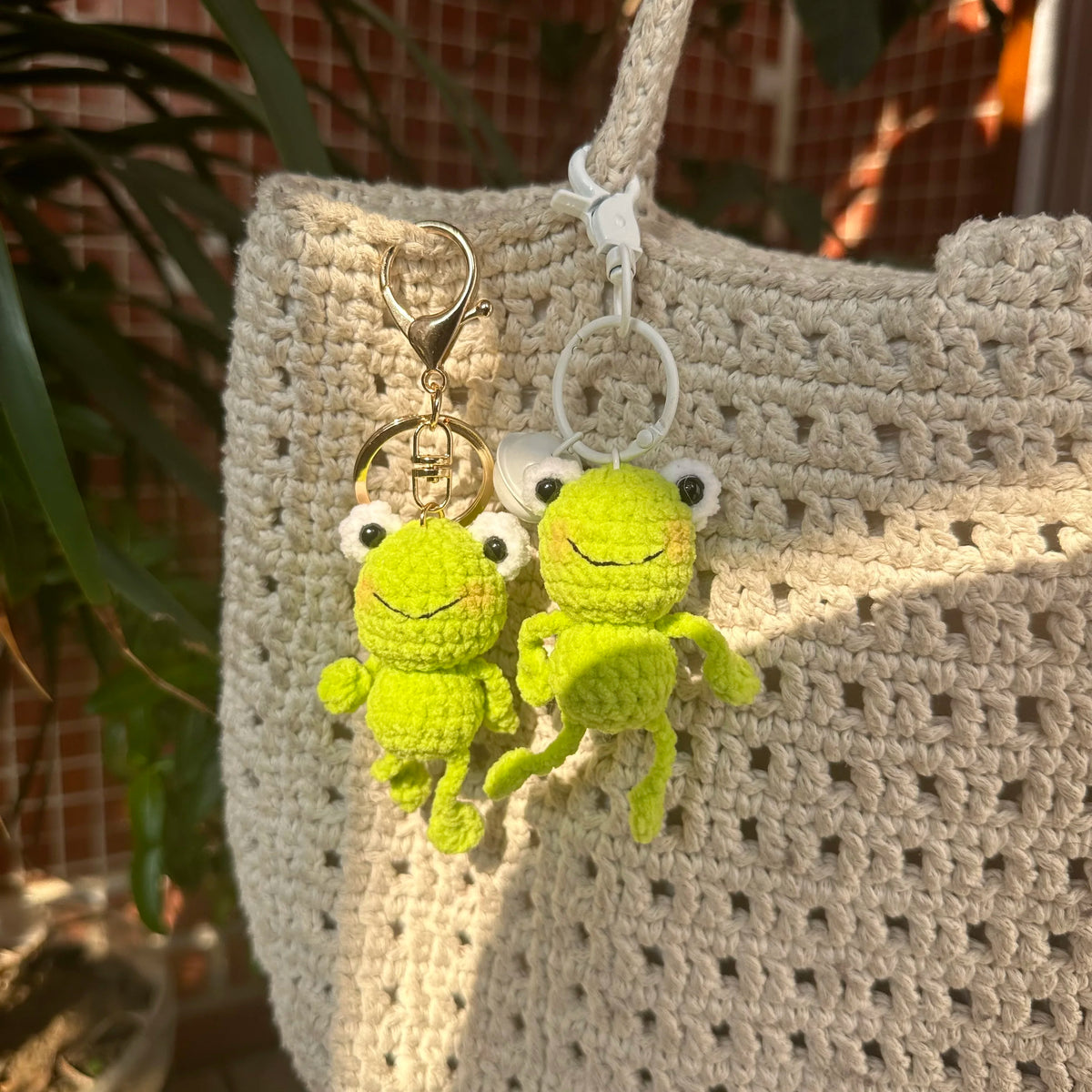 A handmade crochet frog keychain with white and yellow coloring hanging from a knitted bag.