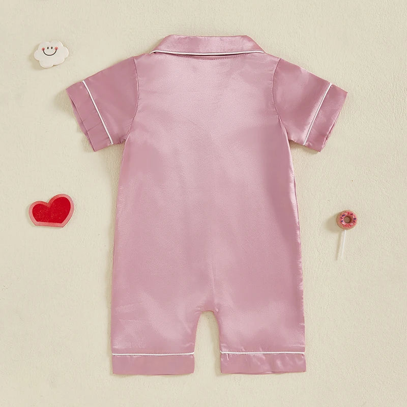 A light pink satin button-up romper sleepwear for toddlers lying flat on a light background.