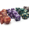 A collection of seven polyhedral dice in various colors and sizes laid out on a white surface.