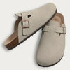 A pair of beige suede cork mules with leather straps and arch support.