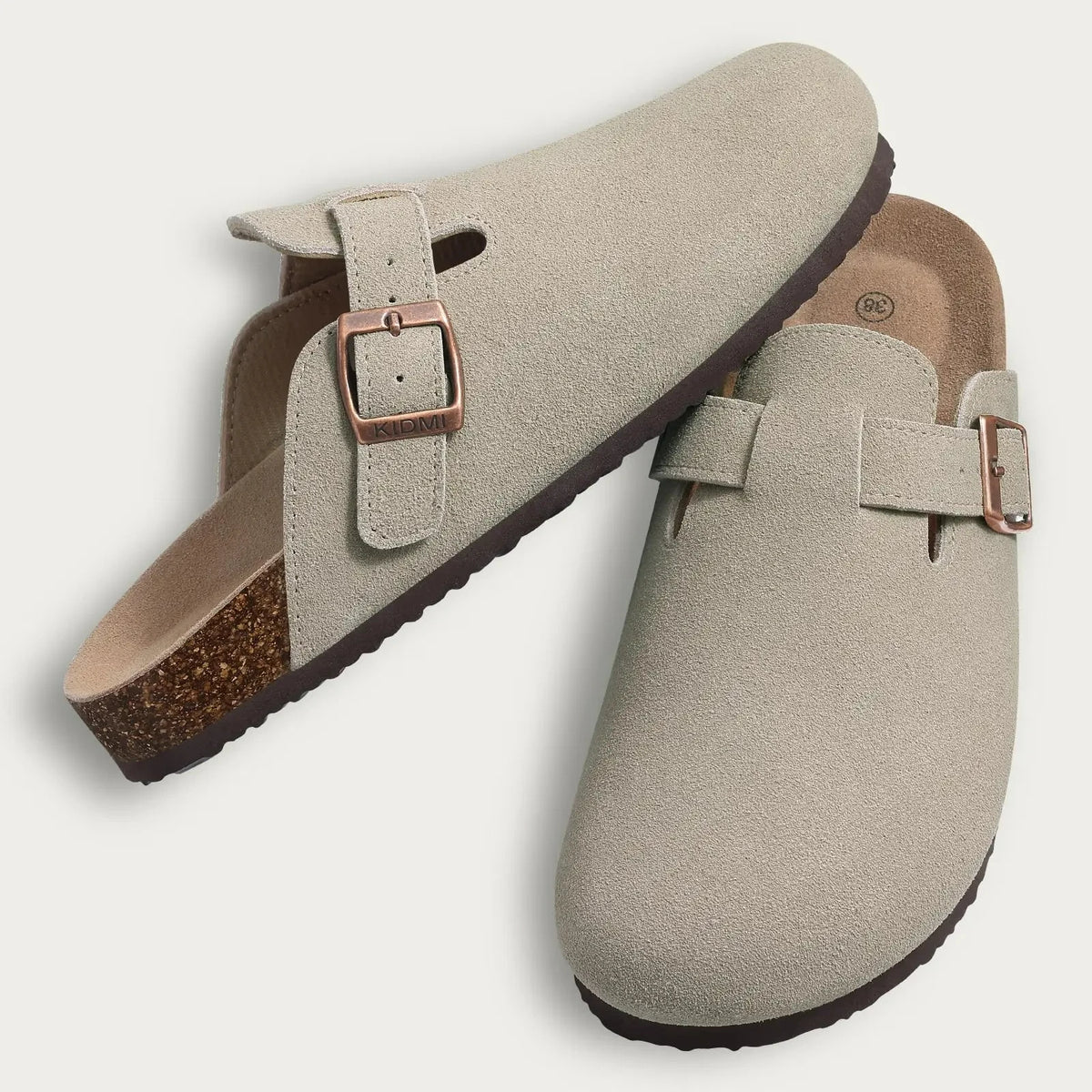 A pair of beige suede cork mules with leather straps and arch support.