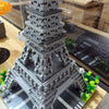A detailed gray LEGO model of the Eiffel Tower built from micro building blocks displayed on a wooden surface.