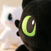 Close-up of a black dragon plush toy with bright green eyes next to a white cartoon figure.