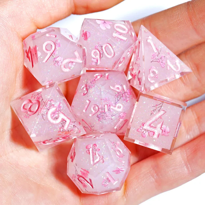 A hand holds a set of pink resin polyhedral dice featuring floral designs.