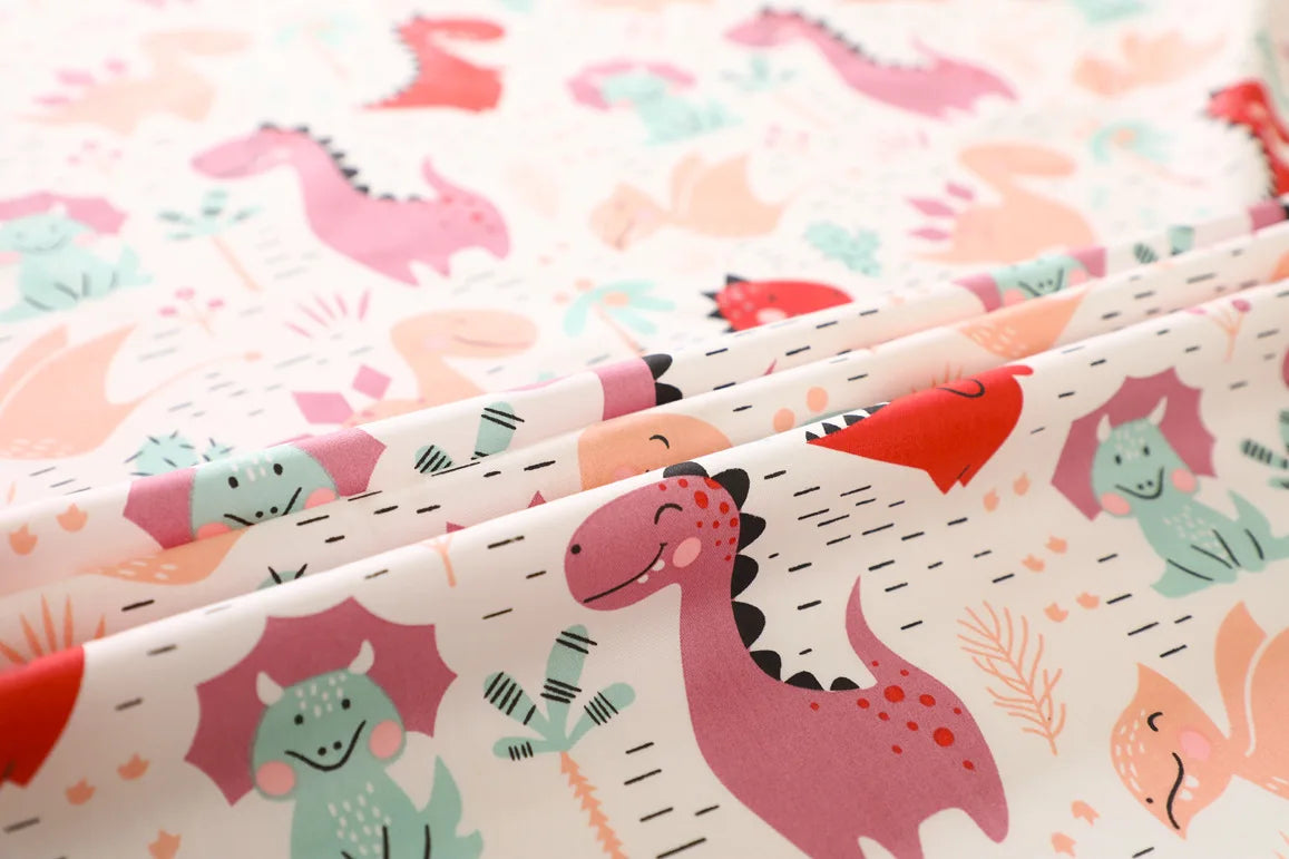 Close-up of a fabric featuring a grid print pattern of pink, teal, and orange dinosaurs for sewing and crafts.