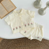 A cream-colored baby cotton shirt and shorts set with a pink flower pattern laid on a white surface.