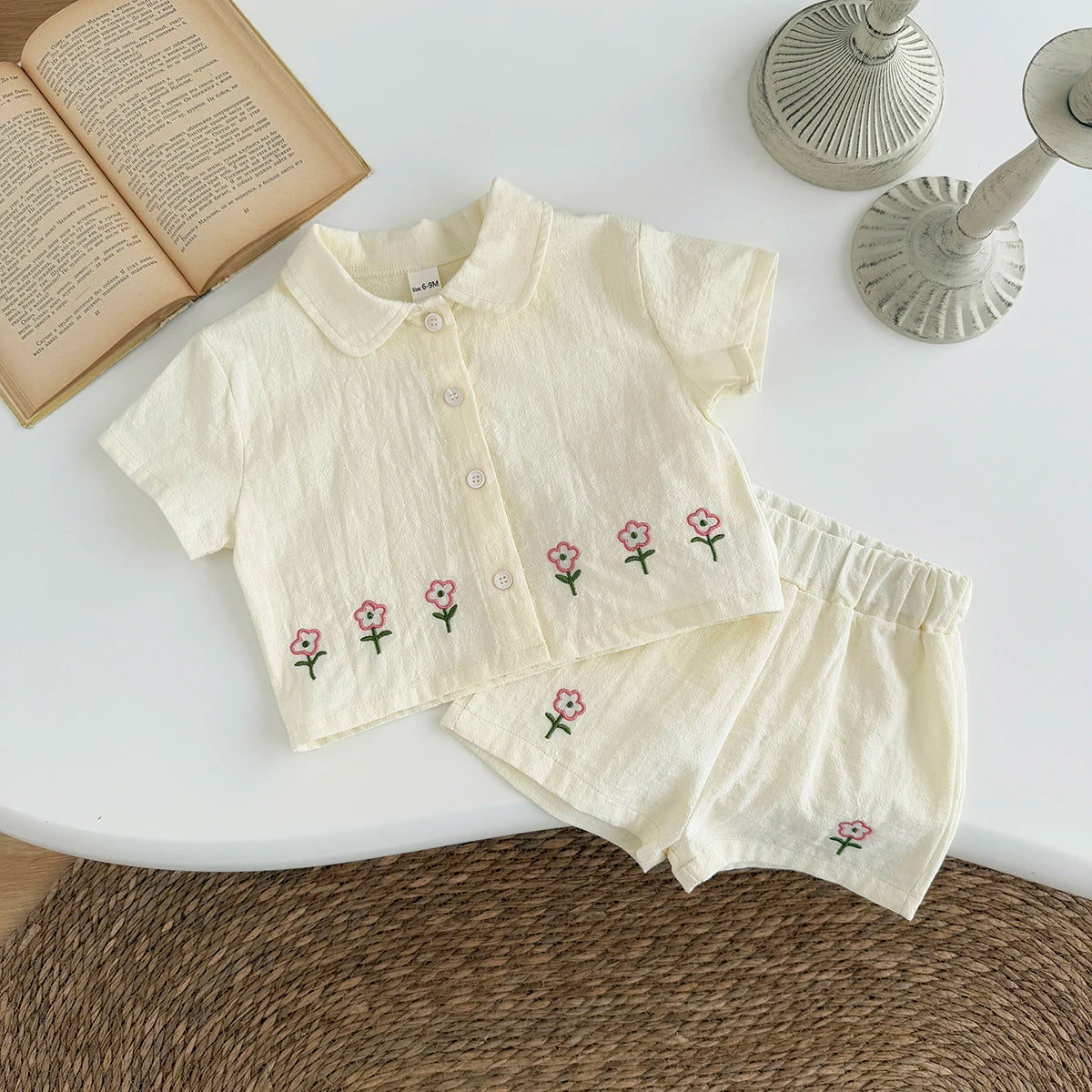 A cream-colored baby cotton shirt and shorts set with a pink flower pattern laid on a white surface.