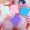 Four square blocks of diamond painting clay in pastel colors pink blue purple and white are arranged on a textured background