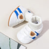 White baby booties with blue stripes and tan faux fur accents shown from the side.